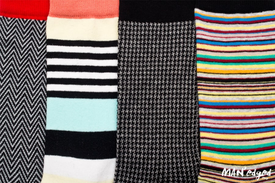left close up of horizontal striped men's socks, thick striped men's socks in light color, houndstooth pattern men's sock, right multi-colored dress sock from related garments