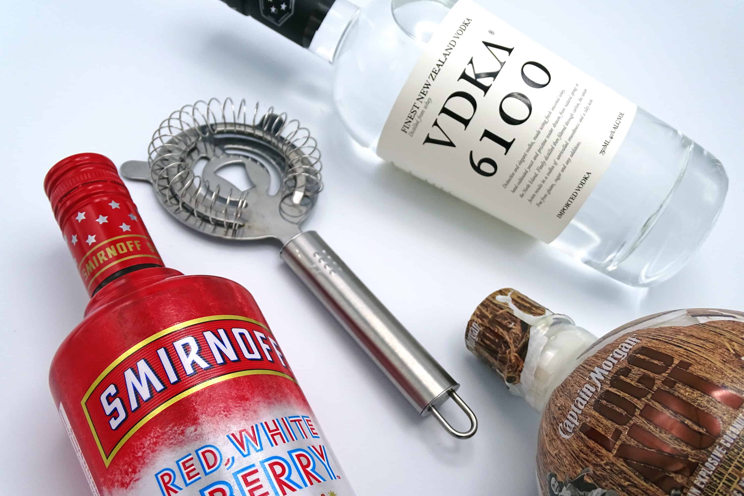 Best cocktails to celebrate 4th of July including: Smirnoff Red, White, and Berry bottle. Cocktail strainer. VDKA 6100 bottle. Captain Morgan Loco Nut bottle. 