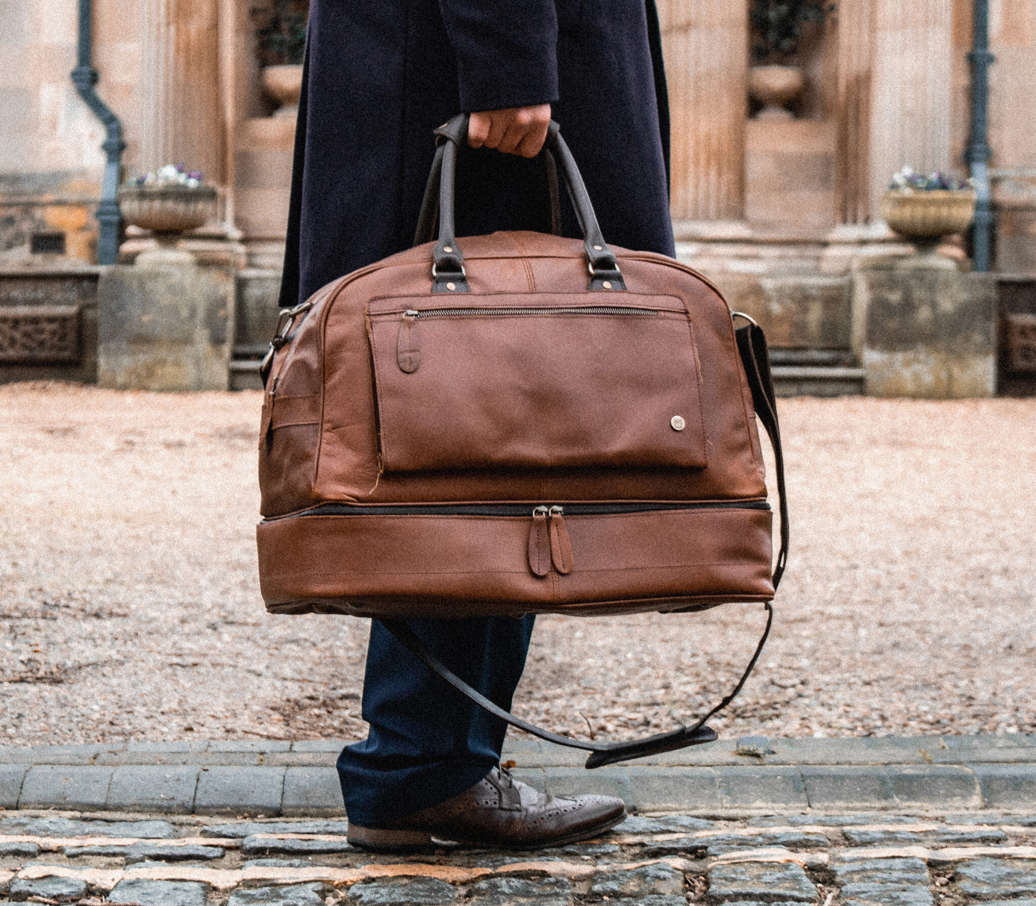 man holding dark brown leather travel bag