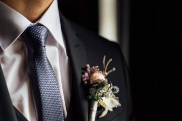 A close-up of a groom's chest to show his outfit's details. He's wearing a vest, boutonniere, and nice tie with a black suit.