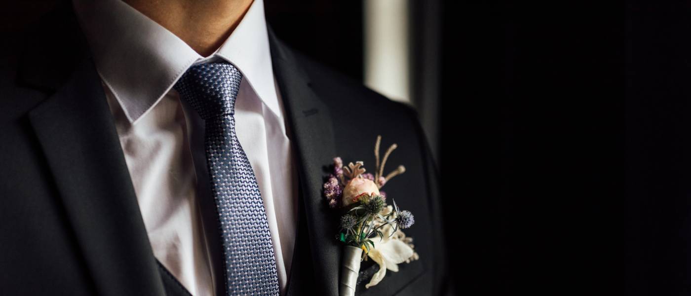 A close-up of a groom's chest to show his outfit's details. He's wearing a vest, boutonniere, and nice tie with a black suit.