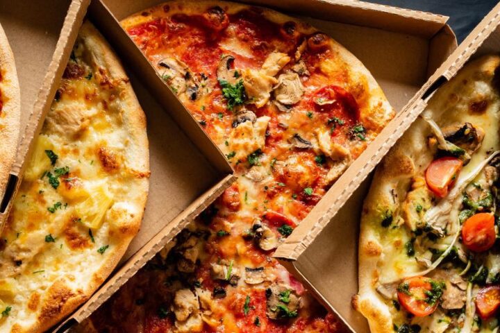 A delicious selection of pizzas in their respective boxes. The boxes are open showing the pizza styles.