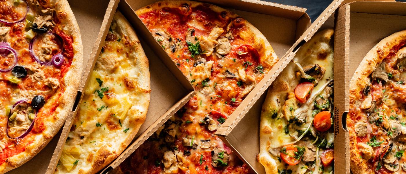 A delicious selection of pizzas in their respective boxes. The boxes are open showing the pizza styles.