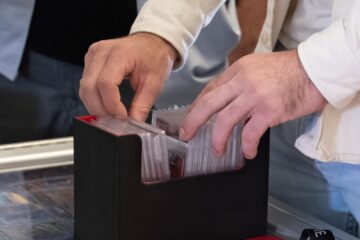 A man thumbing through a black plastic container full of cover-protected collectible sports cards.