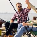 Two guys sitting in camping chairs and fishing on a beach. They're giving each other a big high five as their rods are cast out toward the water.