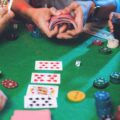 A cropped photo of a group of young people playing poker, with one person showing their hand while another shuffles the deck.