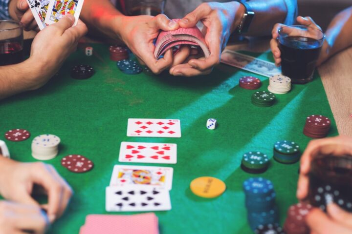 A cropped photo of a group of young people playing poker, with one person showing their hand while another shuffles the deck.