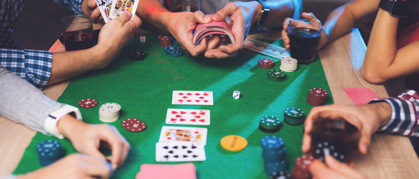 A cropped photo of a group of young people playing poker, with one person showing their hand while another shuffles the deck.