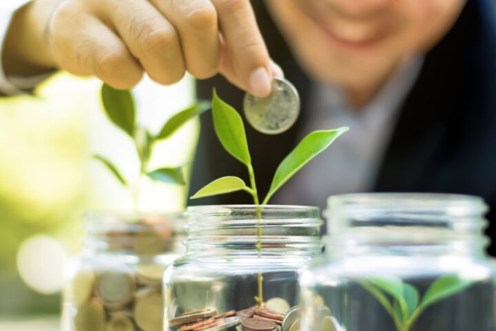 A blurred young man dropping a coin into the middle of three glass jars in a row, each filled with coins and sprouts.