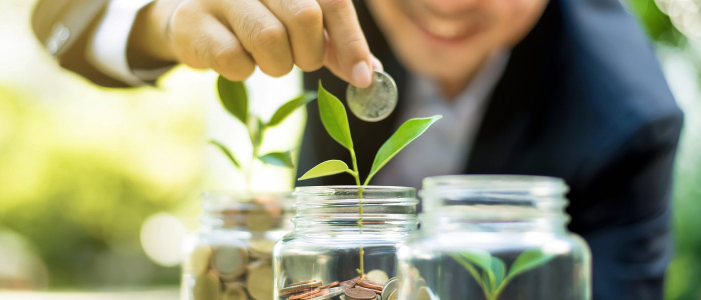 A blurred young man dropping a coin into the middle of three glass jars in a row, each filled with coins and sprouts.