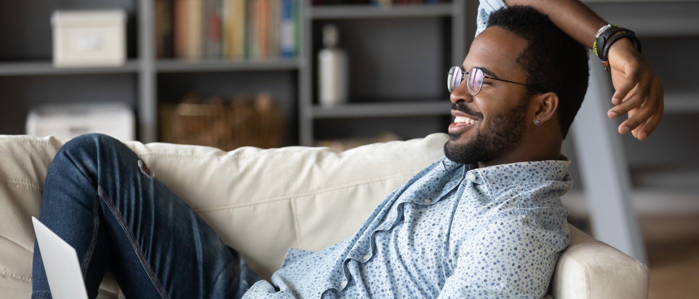 A relaxed man in nice yet casual attire lounging on a white couch in a stylish, well-organized room.