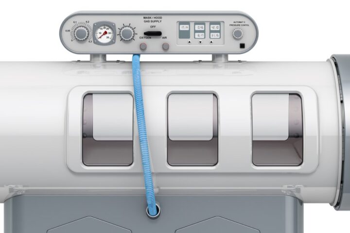 Side view of a hyperbaric oxygen therapy chamber over a white background. The horizontal, tube-shaped chamber is on wheels.