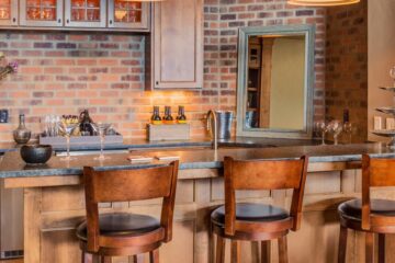 A Tuscan-inspired home bar with a dark stone countertop, faux brick wall, and three wood bar stools.