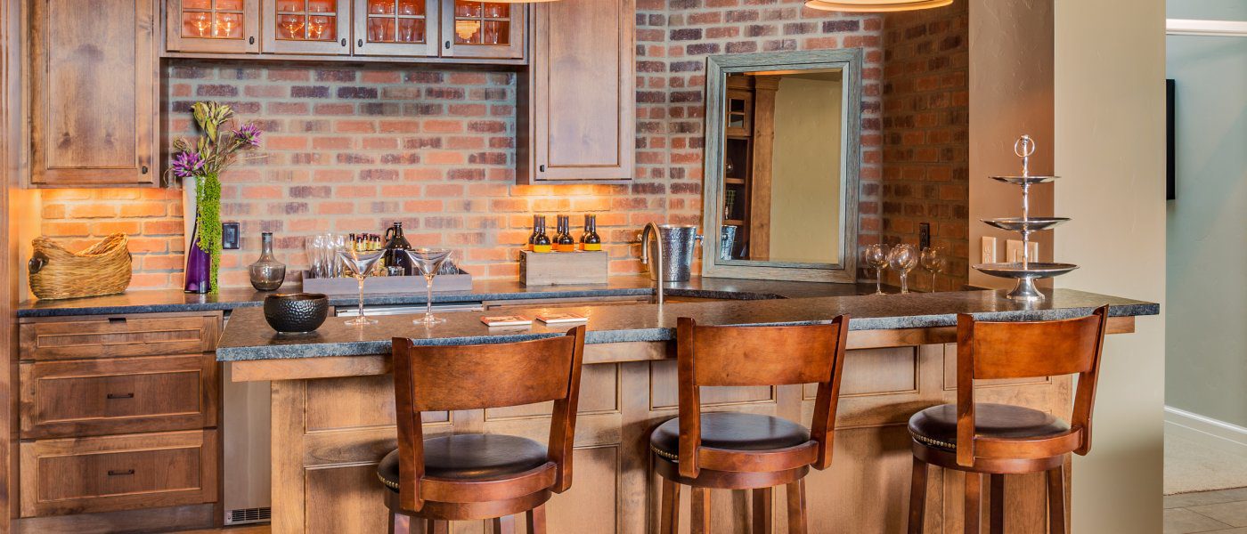 A Tuscan-inspired home bar with a dark stone countertop, faux brick wall, and three wood bar stools.