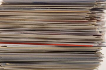 A stack of trading cards sitting on a table against a white background. Some are in casings and others are original format.