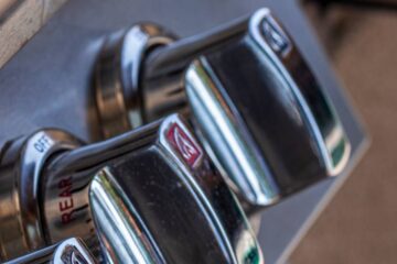 Close-up side view of three knobs on a gas grill. The grill lid is closed, and the grill's metal gleams.