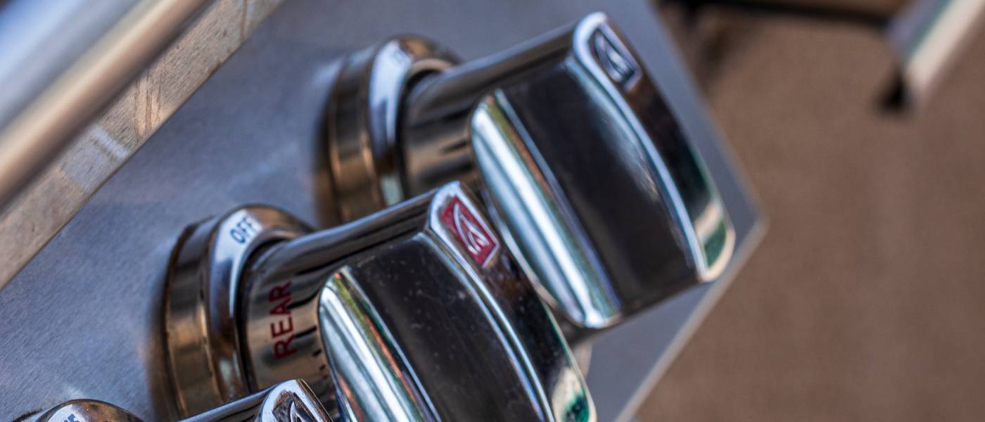 Close-up side view of three knobs on a gas grill. The grill lid is closed, and the grill's metal gleams.