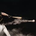 A professional baseball player in a stadium at night, hitting a ball that is speeding away, trailing dust.