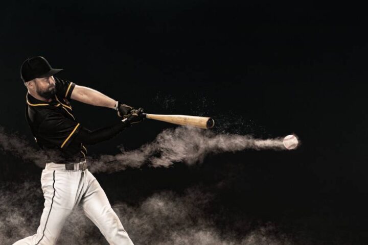 A professional baseball player in a stadium at night, hitting a ball that is speeding away, trailing dust.