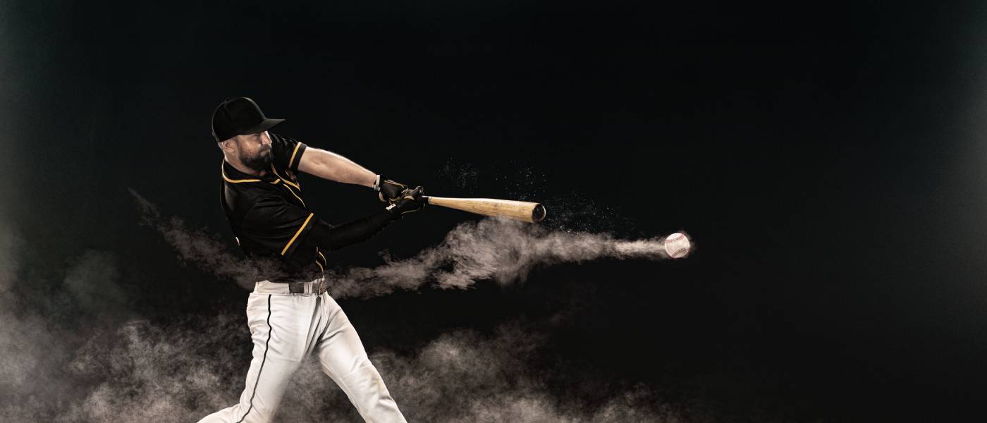 A professional baseball player in a stadium at night, hitting a ball that is speeding away, trailing dust.