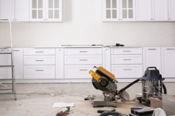 A white kitchen with new cabinetry and silver hardware. The appliances have been removed and there's tools on the ground.