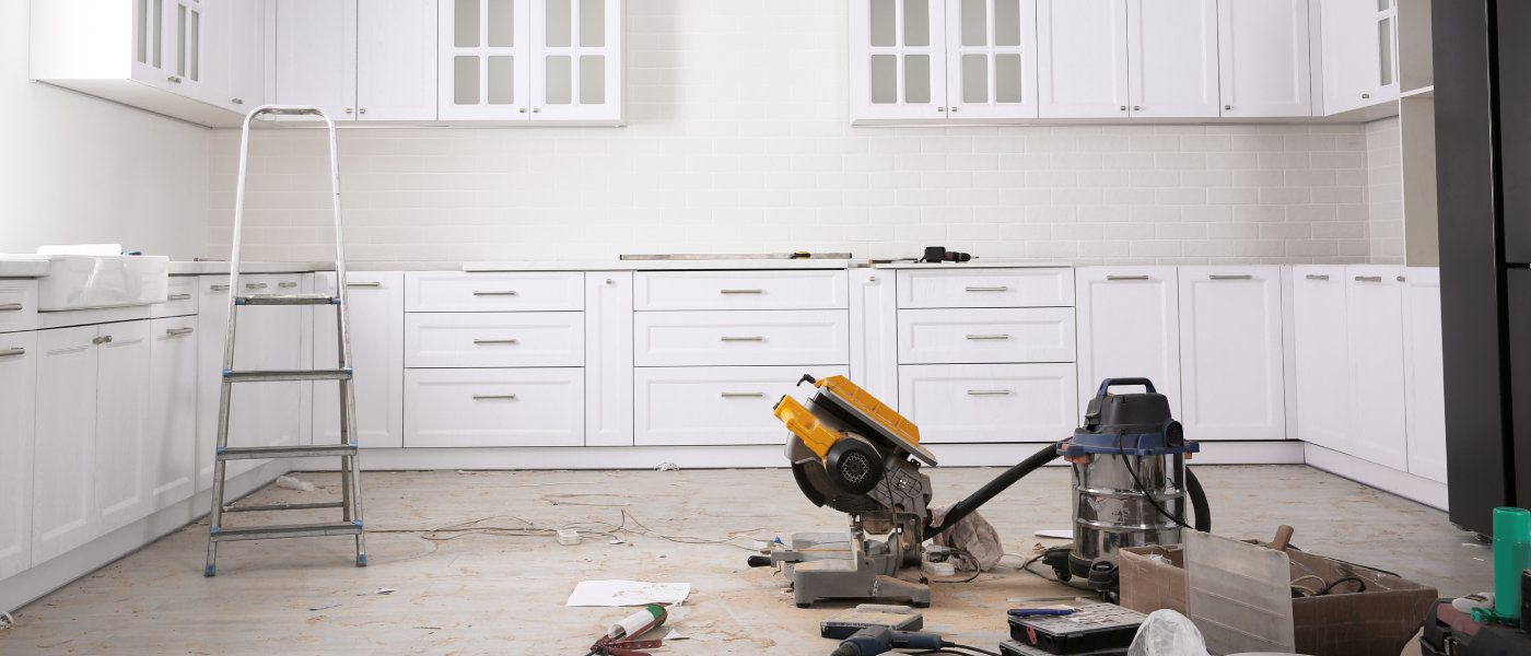 A white kitchen with new cabinetry and silver hardware. The appliances have been removed and there's tools on the ground.