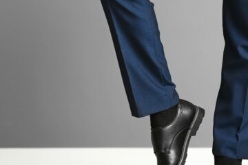 A close-up view of a person showing off the well-ironed legs of their dark blue dress slacks and their black shoes.