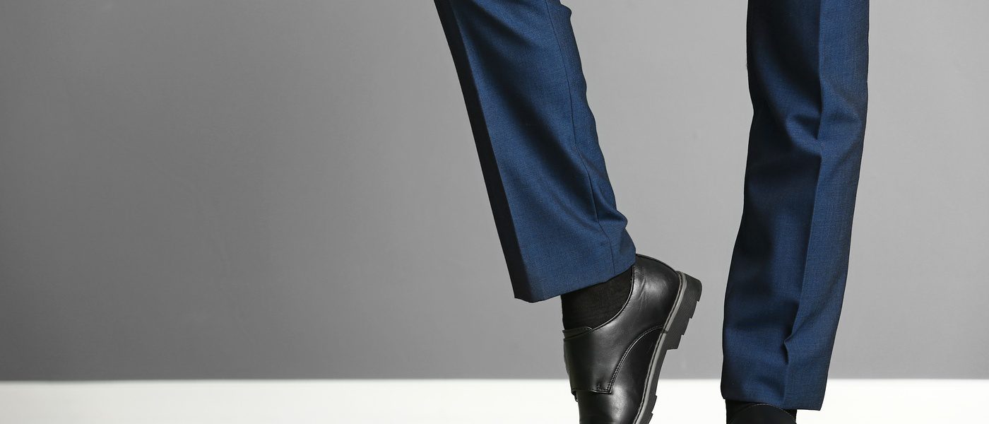 A close-up view of a person showing off the well-ironed legs of their dark blue dress slacks and their black shoes.
