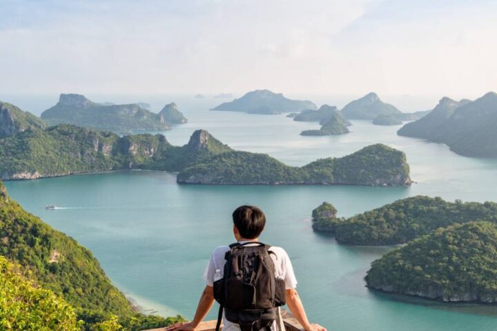 An Asian man standing at an observation deck on the mountain, enjoying the view of the sea and mini islands.