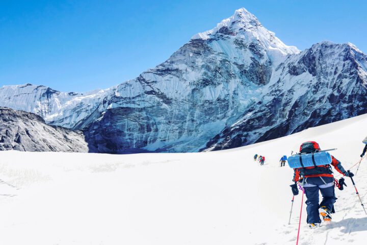 A small group of people wearing proper mountaineering gear trudge through the snow, heading toward Mount Everest.