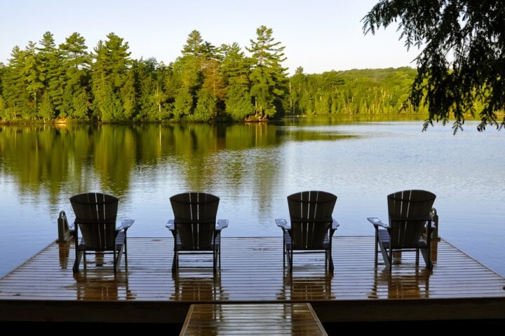 A view looking out on a lake at sunset with a wooden floating dock and four lounge chairs looking out.