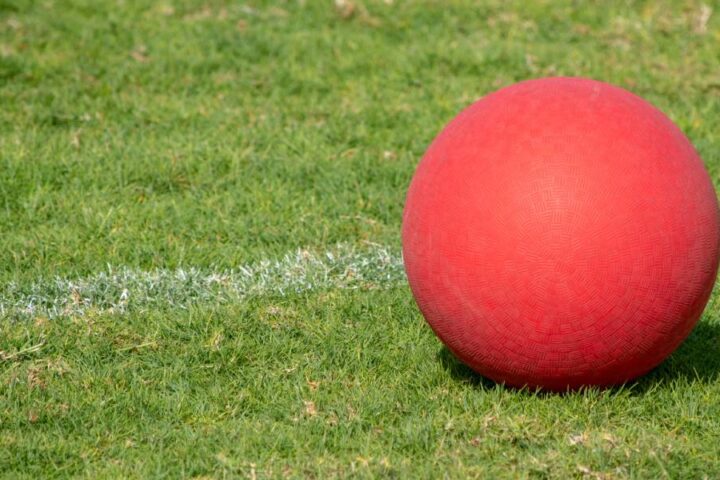 A red kickball resting on green grass field near a white boundary line, suggesting an outdoor recreational play.