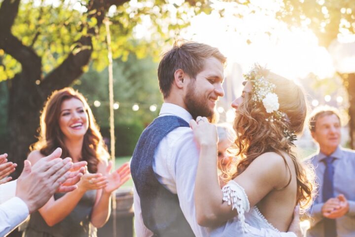 A bride and groom dancing outdoors at a wedding reception while seated guests watch from decorated tables.