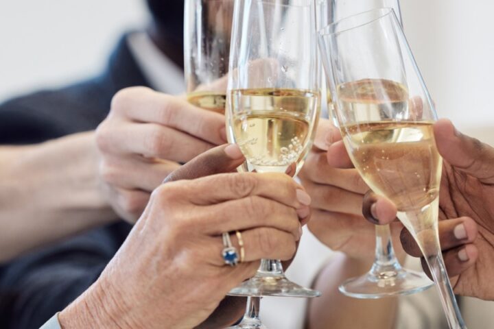 A close-up of a group of people toasting with their champagne glasses. The champagne is bubbly and guests are smiling.