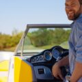 A man with a beard and a blue shirt, piloting a speedboat and looking back over his shoulder and smiling.