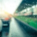 A view of raindrops on a car window. The car appears parked at a train station with other cars nearby.