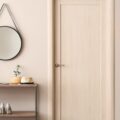 A narrow console table with a shelf holds shoes and plants. Above it hangs a round mirror; beside it is a door.