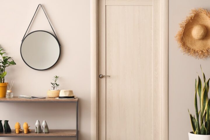 A narrow console table with a shelf holds shoes and plants. Above it hangs a round mirror; beside it is a door.