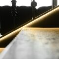 A glowing LED strip traces a dark metal staircase as sunlight enters through the windows in the background.